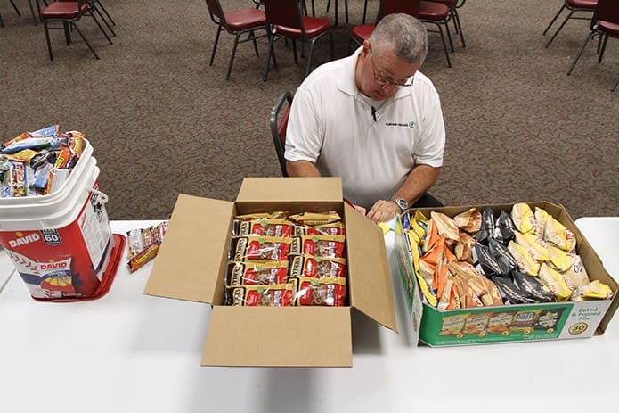 Bob Spidel writes number labels by the food and snack items, so the packers will know how many to put in each care box for the troops. Photo By Michael Alexander