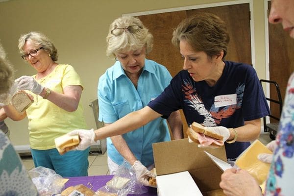(L-r) Mary Lee Duke of Johnson Ferry Baptist Church bags up a ham and cheese sandwich as Holy Family parishioners Susan Higgins and Beckie Adams, bag and handoff sandwiches, respectively. Photo By Michael Alexander