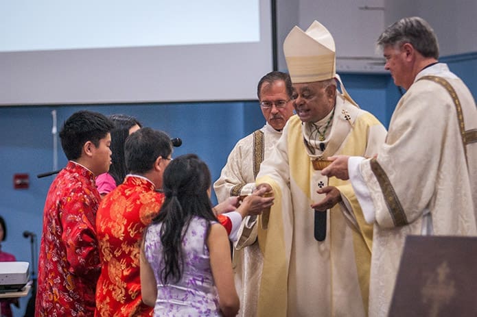 Archbishop Wilton D. Gregory receives the offertory gifts during the Nov. 19 Mass from the Chai family, dressed in traditional Chinese garb. Photo by Thomas Spink