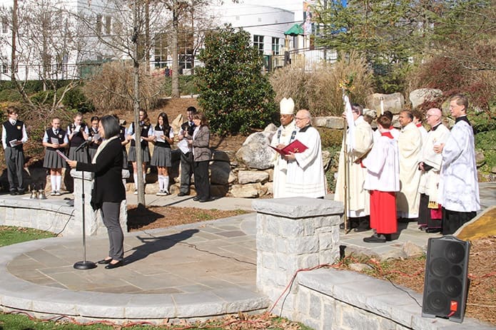 Wanda Yang Temko, standing at the microphone, sings a litany entitled “Hymn for the Holy Year of Mercy” on the green space grounds at Christ the King School, Atlanta, as clergy, middle school students and teachers look on. The brief service was followed by a procession up Peachtree Way to the cathedral for the opening of the Holy Door. Photo By Michael Alexander