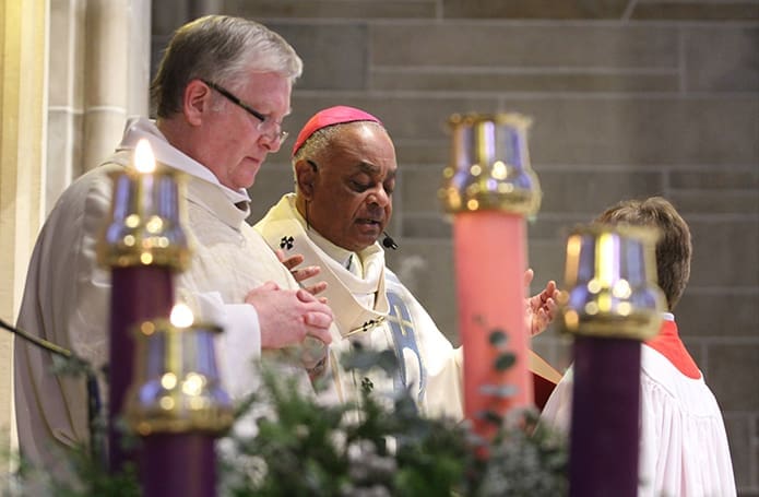 Archbishop Wilton D. Gregory, second from left, is centered between the Advent wreath candles as he conducts the opening prayer during the Mass for the solemnity of the Immaculate Conception at the Cathedral of Christ the King, Atlanta. Assisting on the altar with the archbishop is Deacon John McManus. The Mass followed the opening of the Holy Door on the Peachtree Road side of the cathedral. Photo By Michael Alexander