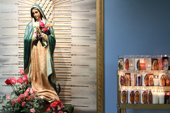 Votive candles burn on a stand next to a statue of Our Lady of Guadalupe inside Our Lady of the Americas Mission. Photo By Michael Alexander