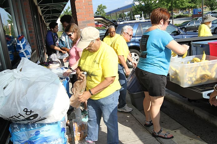 Before they go out on the street, (clockwise, from rear right) Pauline Bullard-Moore and Lauren Russell of St. Thomas the Apostle Church, Smyrna, position the bends for sorting as Hope Douglass of Buckhead Church, Atlanta, fills a bend with bananas and Josie Poventud of St. Thomas the Apostle Church fills a bag with water and a sandwich before she passes it down the line to the other volunteers to be filled with other items. Bullard-Moore is one of the five founding members of the Just Faith Feed the Hungry ministry. Photo By Michael Alexander