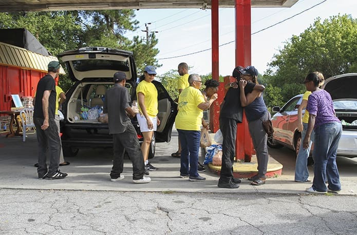 The volunteers make their second of three stops at a vacant gas station at the corner of Donald Lee Hollowell Parkway and Yates Drive NW. The distribution of food is only part of the Just Faith Feed the Hungry ministry. Since it’s been around five and half years, many of the volunteers have formed a bond and friendship with the people on the street. They greet each other and converse until it’s time to move on to the next stop. Photo By Michael Alexander