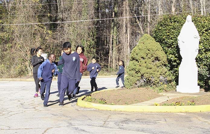 Second-grader John Sisoun, foreground left, and seventh-grader Soe Reh, foreground right, lead their coach, Leann Martin, far left, and fellow Kilometer Kid participants on a practice run through the St. Peter Claver Regional School parking lot. Photo By Michael Alexander
