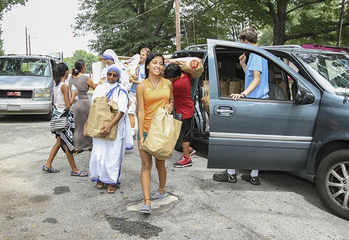 While other volunteers unload sacks of potatoes, 15-year-old Grecia Tierrafria, foreground center, and Missionaries of Charity Sister Leo Grace, left, carry bags of food from a volunteer’s vehicle to the residents of Colony South mobile home park in southeast Atlanta, where Tierrafria lives with her seven siblings and parents. The sisters distribute food there on special occasions like Christmas or Easter, and the upcoming canonization of Mother Teresa became another reason to do so on Aug. 27. Photo By Michael Alexander