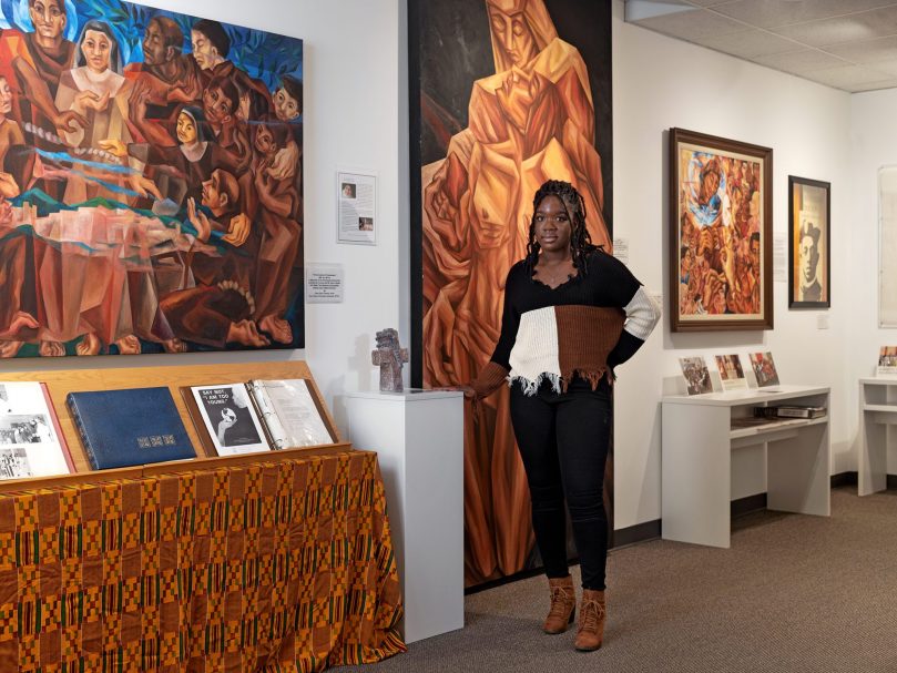 Newman Scholar of the Year Betoyah Dorzema stands with her sculpture entitled, “A Cold Prayer in Your Woods,” inside the new Archbishop James Patterson Lyke Memorial Gallery at Lyke House.