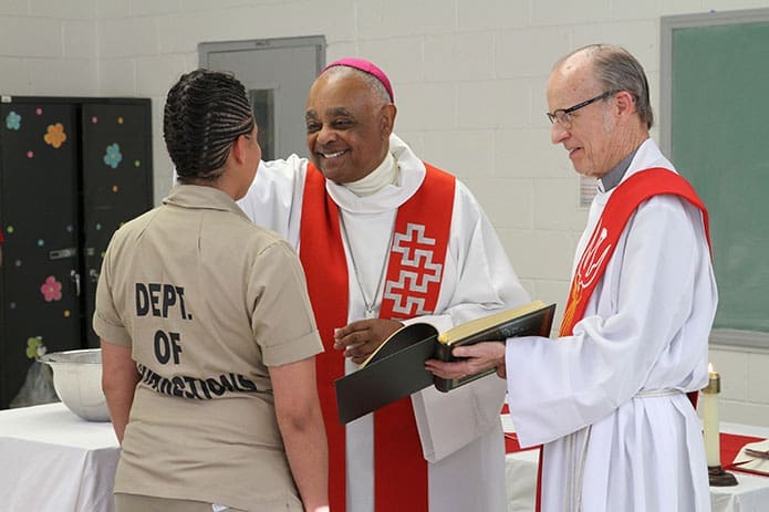 Archbishop Wilton D. Gregory, center, confirms Amy Ruiz, one of the five female inmates he confirmed during a May 2 liturgy at Arrendale State Prison, Alto. The 29-year-old mother of four children took Guadalupe as her confirmation name. Looking on is Deacon Bernard Casey of St. Thomas Aquinas Church, Alpharetta. Archbishop Gregory also baptized an inmate. Photo By Michael Alexander