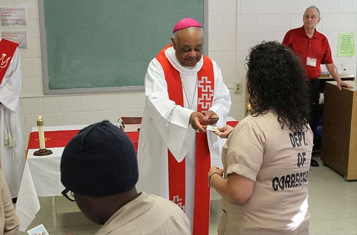 Archbishop Wilton D. Gregory passes out St. Michael the Archangel prayer cards to all the inmates. He also presented a book of the New Testament Psalms to those who were baptized and confirmed. Photo By Michael Alexander