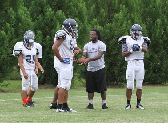 Running backs coach Tremell Callaway, second from right, shows the runners how they should take the handoff from the quarterback during an August 14 practice. Photo By Michael Alexander