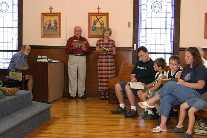 (L-r) Rick Hansard, on piano, is joined by Herb Leinberger and Susan Walker as they sing the offertory hymn "Here I Am Lord." On the front pew are members of the Price family. Photo By Michael Alexander