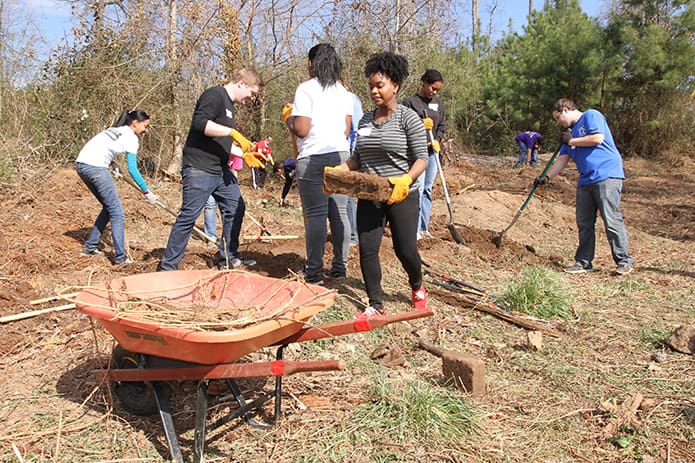 Rachel Lohan, a junior microbiology major from Atlanta, walks toward the wheelbarrow with some debris as her fellow University of Georgia students participate in a grounds cleanup day at Oasis CatÃ³lico Santa Rafaela, inside the Pinewood Estates North mobile home community, Athens. Photo By Michael Alexander