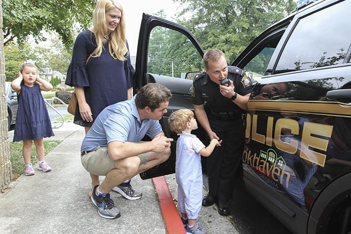(R-l) Brookhaven Police Department’s Major Brandon Gurley shows 2-year-old Thomas Gioia how it sounds to speak over the police loudspeaker, as his parents Tom and Ashlyn look on. In the background Thomas’ 4-year-old sister, Eleanor, covers her ears from the noise. Photo By Michael Alexander