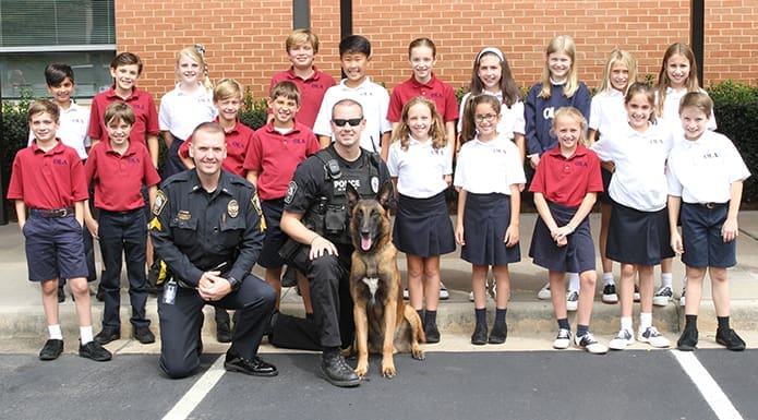 (Front row, kneeling) Brookhaven Police Department Sgt. Jake Kissel, K9 handler Officer David Fikes and full-service police work dog, Dano, pose for a photograph with Kathryn Berg’s fifth grade class at Our Lady of the Assumption School. Sgt. Kissel, who was adopted by the entire fifth grade, which includes two other classrooms, invited police K9 handler Officer Fikes and Dano, a Belgian Malinois, as his special guests. Photo By Michael Alexander