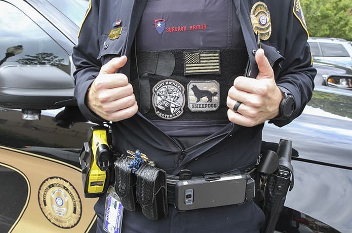 Sgt. Jake Kissel, of the Brookhaven Police Department, opens his uniform shirt to reveal the bulletproof vest that bears patches including an American flag, a sheepdog and St. Michael the Archangel, the patron saint of first responders, including police officers. In some circles police have been compared to sheepdogs guarding the sheep, which is the community. Photo By Michael Alexander