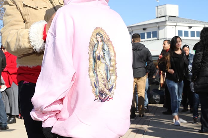 People walk around Heritage Point Park during the Our Lady of Guadalupe festival, which featured food vendors, music and dancing, as a mother adjusts the zipper on her daughter’s fleece that featured an imprint of Our Lady of Guadalupe on its backside. Photo By Michael Alexander