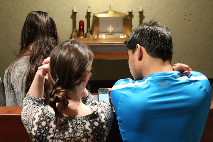 Students-at-the-Georgia-Tech-Catholic-Center-conduct-a-prayer-during-adoration-with-the-use-of-a-smart-phone.-Not-only-is-technology-and-social-media-encouraged-to-keep-congregations-up-to-date-but-technology’s-use-is-also-suggested-as-a-possible-teaching-tool-when-it-comes-to-faith-formation.-Photo-By-Michael-Alexander