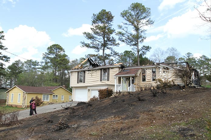 Deacon Norm Keller and his wife Barbara comfort one another as they stand in the driveway of their Marietta home that was destroyed by flames after a Cessna aircraft crashed in the couple’s front yard March 24. The Kellers were at their parish, St. Joseph, attending the Stations of the Cross when the fatal crash occurred, killing the pilot. Photo By Michael Alexander