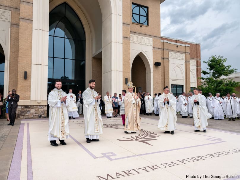 Four of the five newly-ordained priests, from left, Jared Kleinwaechter, Arturo Merriman, Joseph Nguyen and Colin Patrick stand with Archbishop Gregory John Hartmayer, OFM Conv., and are greeted with applause following the June 1 ordination to the priesthood. Photo by Johnathon Kelso