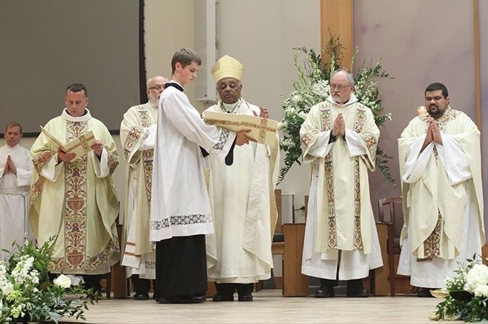 Seminarian Dan Fitzgerald holds the book as Archbishop Wilton D. Gregory conducts the prayer of dedication at Prince of Peace Church, Flowery Branch. Also following along and standing on the altar are (second from left to right) Father Eric Hill, pastor, Deacon William Donohue, Deacon Tom Walter and Father Luis Alvarez, parochial vicar. Photo By Michael Alexander