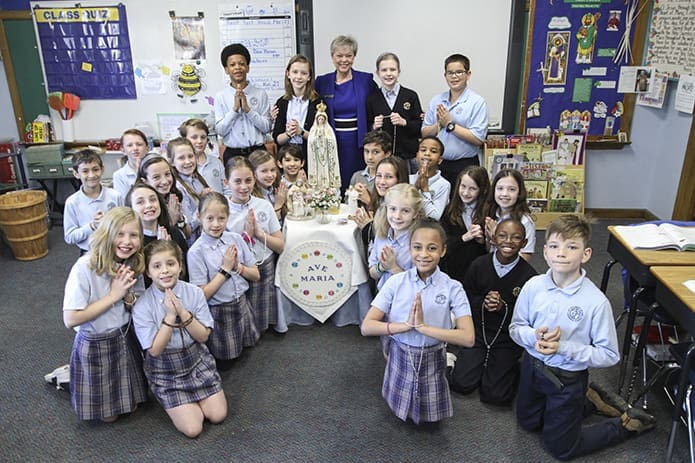 Melody Summers, background center, poses for a photograph with her fourth-grade students around a small Marian altar that normally occupies the corner, background right, by the entrance to the classroom. Miss Summers has a great devotion for the Blessed Mother and praying the rosary, something she has often shared and passed on to her students over the years. Photo By Michael Alexander