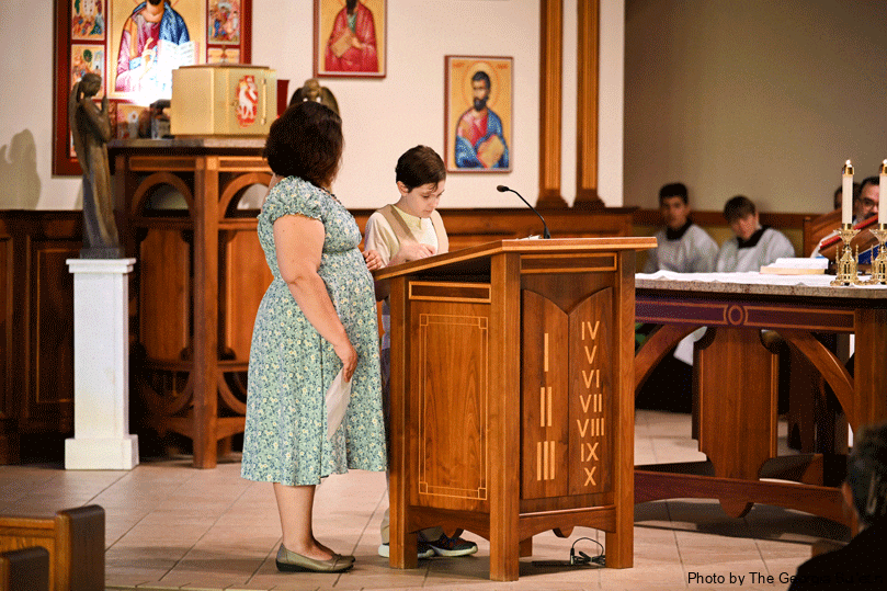 Eleven-year-old Kenneth Henderson offers a reading at St. John Vianney's first sensory Mass. His mother Reyna Ochoa stands by to support him. The sensory Mass is designed especially for parishioners with autism, Down syndrome, intellectual disabilities, the elderly or anyone with sensory sensitivities. The shorter Mass featured dimmed lighting, soft music and no bells. Photo by Julianna Leopold