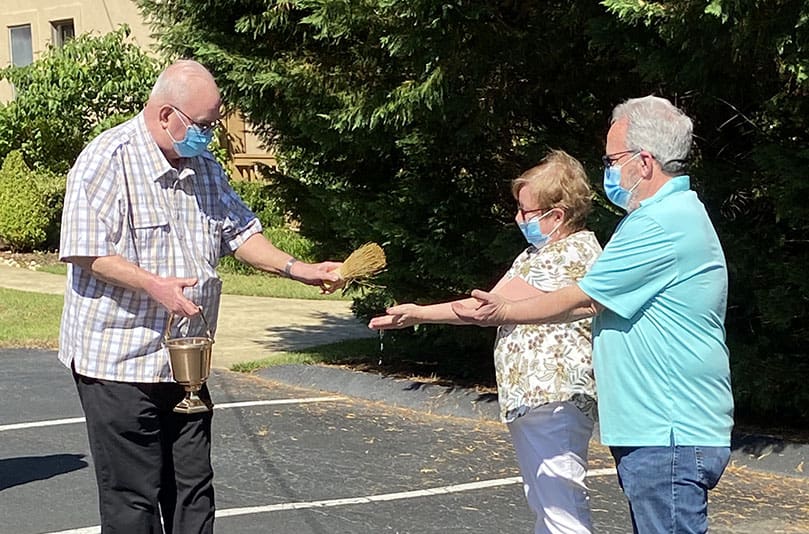 Missionary of Our Lady of La Salette Father John Gabriel, left, blesses the hands of Barb and Dave Smith. Dave is a member of the Adult Mission Ministry and he coordinated construction of the garden. Barb is one of the volunteers who helps with the garden. Photo By Karen Miller.