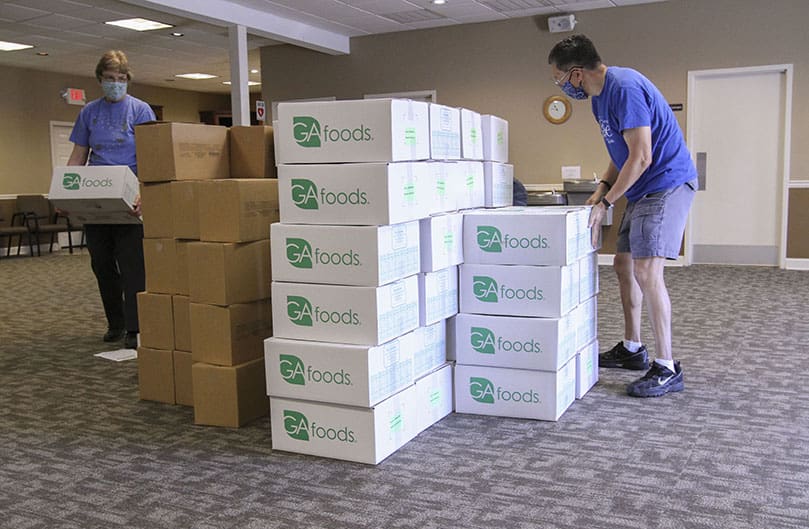 Volunteers Eleanor Dudek, left, and David Hom arrange boxes containing produce, butter, cheese, fruit, milk and diced chicken. The boxes were part of a 4,381-pound haul of produce and food dropped off by the Atlanta Community Food Bank July 13. Photo By Michael Alexander