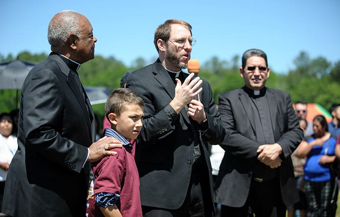 Father Timothy Gallagher, pastor of St. Bernadette Church, invites 8-year-old Tony Pizano to join Archbishop Gregory and building committee members for the official groundbreaking of a new parish center. Deacon Jose Orellana is shown right. Photo By Gibbs Frazeur