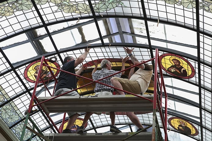 (L-r) Frank Llorens Jr., Frank Sr. and Robert Zortea install the fourth of four 30-by-71.5-inch panels that comprise the new major icon in the refurbished vaulted glass skylight. The Llorens are the proprietors of Llorens Leaded Art Glass, Inc., Winder, which has been in existence for 104 years. Frank Sr.’s father, Joseph Victor Llorens, was the original designer of the vaulted glass ceiling when it was the mansion of the late Coca-Cola co-founder Asa Candler. Photo By Michael Alexander