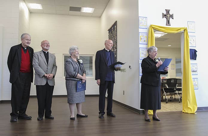 Sister of Mercy Sally Condart, far right, shares some remarks with the audience on hand for the blessing and dedication of the school’s Mercy Conference Room behind her. Standing with Sister Sally are (l-r) former St. John’s pastor Father Richard Morrow, former parochial vicar Father Steven Yander, Sister of Mercy Kathleen Lyons, and former parochial vicar Father John Adamski. Photo By Michael Alexander