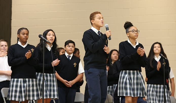 Nathan Haydel, holding the microphone, and Jada Sardin, right, lead their fellow eighth-graders in singing the song entitled “Higher.” Photo By Michael Alexander