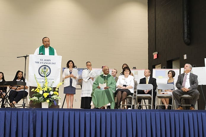 Father Michael Onyekuru, at podium, pastor of St. John the Evangelist Church, addresses the crowd of alumni, benefactors, parents, students and staff present for the opening of the parish school’s new Enrichment Center. Photo By Michael Alexander