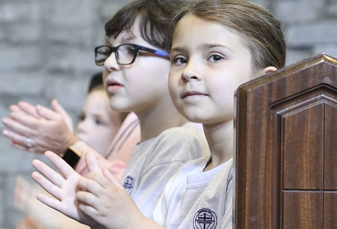 (Foreground to background) Amanda Main and Charlie Kemp, first-graders at St. Jude the Apostle School, Atlanta, clap to the music during Praise and Worship, held the morning of May 17. Photo By Michael Alexander