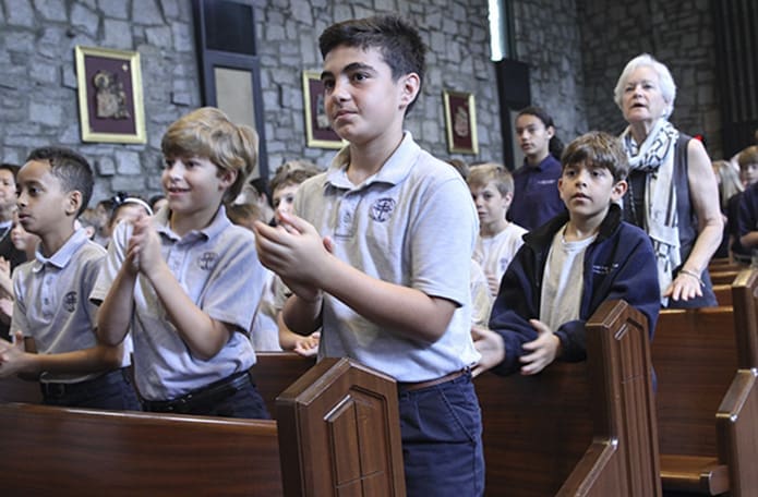 (Foreground to background, from center) Third-graders MJ Arabia and Joe Chiaffredo and Molly Strozier, third-grade assistant teacher, stand as the band performs one of nearly a dozen songs giving glory and thanks to God. Photo By Michael Alexander
