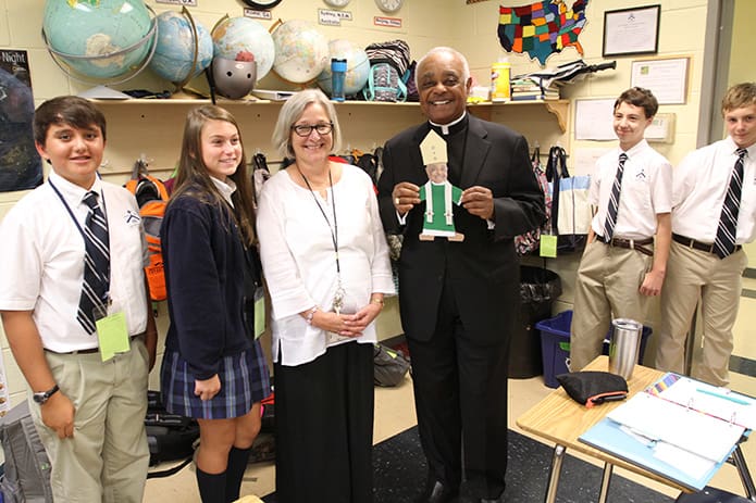Archbishop Wilton D. Gregory, right center, holds a cutout of a âflat Wiltonâ that was made and given to him by middle school teacher Marti Miller, left center, as he visited classrooms following the 70th anniversary Mass. The students on hand include (l-r) seventh-graders Eli Van Meter, Taylor Abbott, Jacob Bruce and eighth-grader Gabriel Jones. Photo By Michael Alexander
