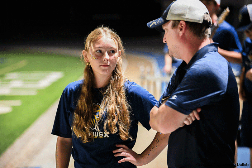 Zoe Leiner, senior drum major for the Marching Golden Lions, left, and Ian LaBreck, band director, right, chat before the halftime show at St. Pius X High School.  Photo by Julianna Leopold
