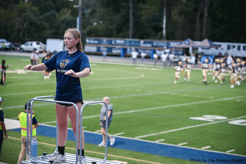 Zoe Leiner, senior drum major, stands atop her bandstand and conducts while the St.  Pius X  football game plays out behind her.  Photo by Julianna Leopold