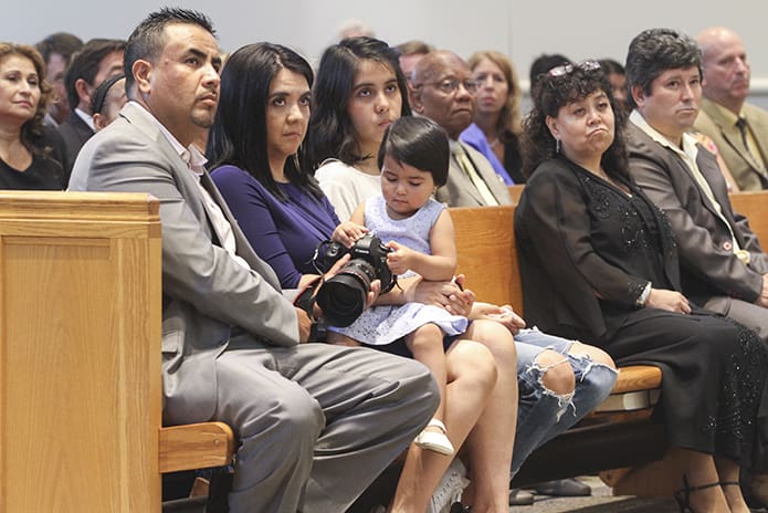 Two-year-old Alessandra Suarez plays with her fatherâs camera as her parents Jose and Maria and her sister Montserret are attentive to Bishop Luis Zarama during his homily. As members of Immaculate Heart of Mary Church, the Suarez family became friends with Father JesÃºs David Trujillo-Luna when he was assigned to the Atlanta church. Photo By Michael Alexander