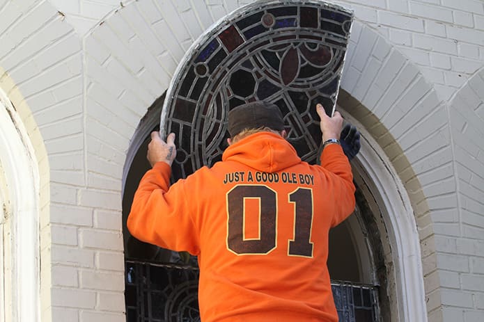 Michael Farmer, an employee of Foothill Sand To Glass, works from the outside to remove one of the stained glass window panels from St. Joseph Church, Athens. On the other side of the window is company owner Avery Wooten. The Jan. 13 effort marked the removal of the last three large windows, looming approximately 10 feet in height, from the church. Photo By Michael Alexander