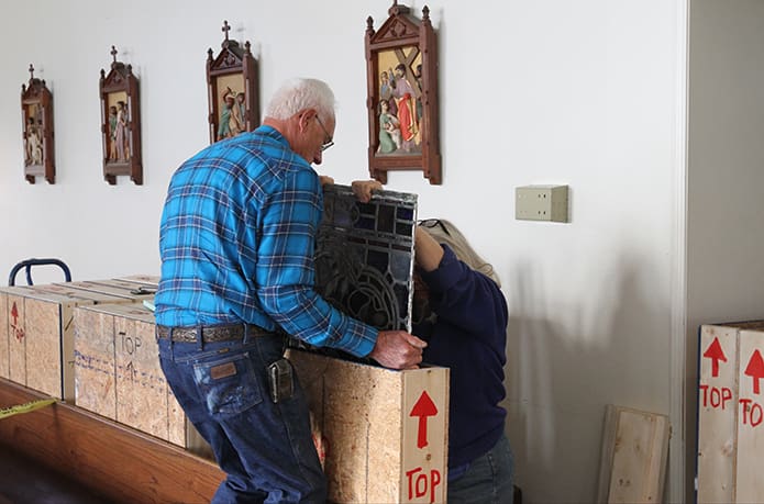 Bernard Wysocki, left, carefully lets a stained glass panel down in its protected wooden crate with help from Marianne Parr, a local stained glass artist who is restoring the windows. Photo By Michael Alexander