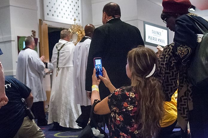 A young woman takes a photograph in the main corridor at the congress after the Blessed Sacrament moves by in a reverent procession. Photo by Thomas Spink