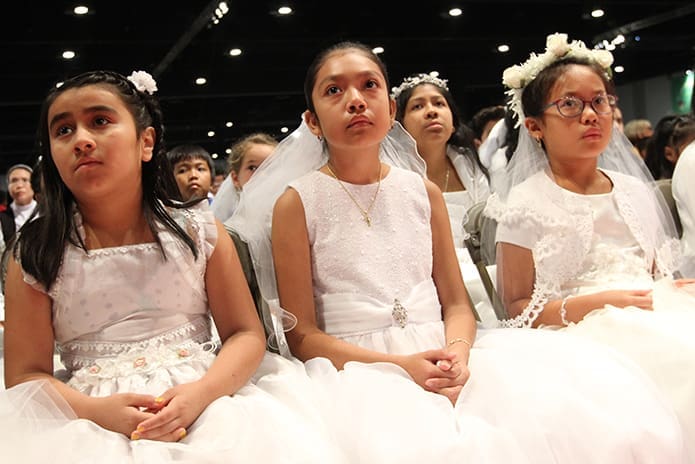 (L-r) Dressed in their first holy Communion dresses, (l-r) Heidy Juarez and Helen Ramirez of St. Paul of the Cross Church, Atlanta, and Allison Nguyen of St. Monica Church, Duluth, listen to a Scripture reading from the front row during the Benediction service. Photo By Michael Alexander