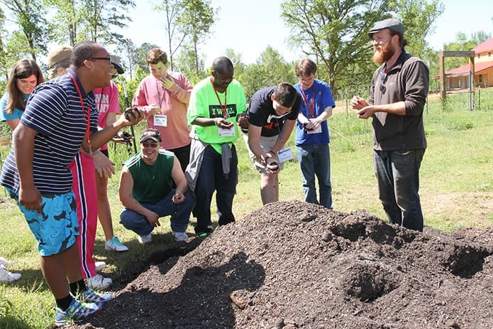 Nathan Fussell, far right, a famer at Camp Twin Lakes, gives campers an opportunity to feel and smell a pile of soil before taking them through the greenhouse and the vegetable garden. Photo By Michael Alexander