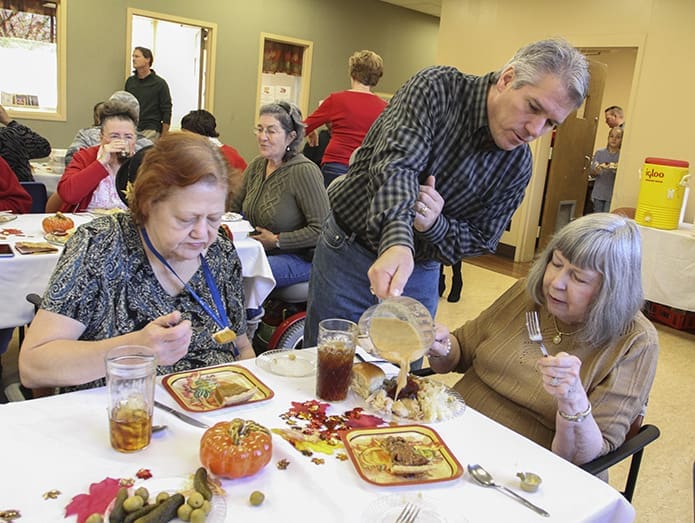 Dave Springstead, center, pours some gravy over Mable Dawsonâs mashed potatoes as Carol Varner, left, eats pie for dessert. Although his wife and daughter have volunteered in previous years, this was Springsteadâs first time working at the dinner. Photo By Michael Alexander