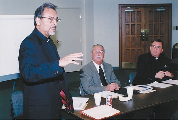 In a photo from 2000, Msgr. Arturo Bañuelas, standing, addresses an audience of Atlanta priests who minister to Hispanics in North Georgia during a meeting about the El Paso immersion program’s first summer experiences. Looking on are Gonzalo Saldaña, center, former director of the archdiocese’s Hispanic Apostolate, and Father David Talley, who was the chancellor and vocations director for the Archdiocese of Atlanta at the time.