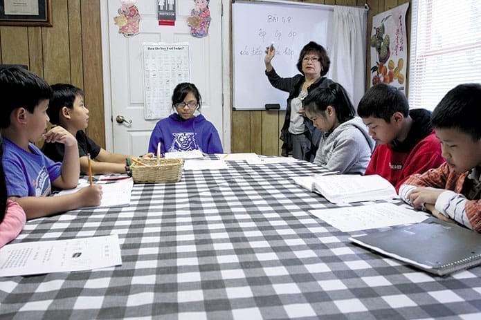 Photo: Cultural enrichment instructor Quyen Nguyen, standing, teaches the youth class words and phrases in Vietnamese as (clockwise, from left) Huy Thang Dang, Lucas Long, Dong Bach, Sandra Nguyen, Tan Bach and Kevin Nguyen listen and look over their material.