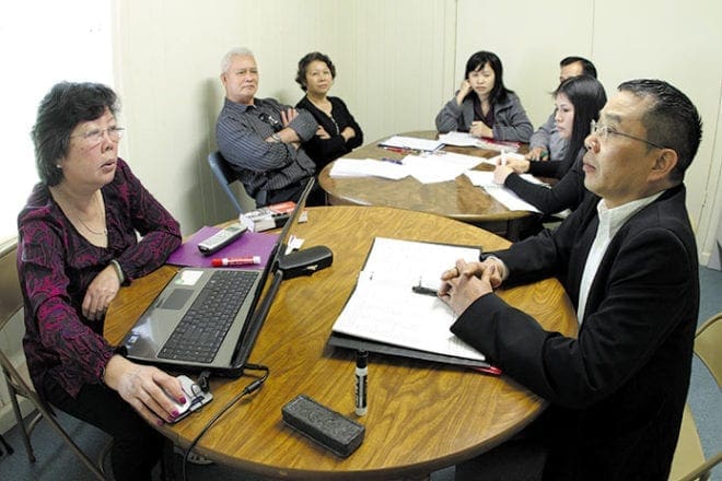 Photo: English and citizenship prep instructor, Thuy Le, foreground left, practices posing a series of citizenship questions to Bac Pham, foreground right, as the rest of the class observes.