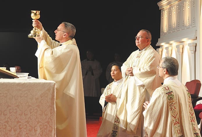 Auxiliary Bishop Luis Zarama elevates the chalice during the consecration as Auxiliary Bishop David Talley, standing, transitional deacon Richard Vu, kneeling left, and permanent deacon Carlos Garcia, kneeling right, look on from behind.