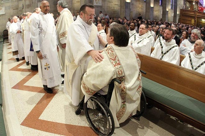 Deacon Al Gallagher, standing, of Holy Family Church, Marietta, extends the Kiss of Peace to Deacon Francis Head Jr. of St. Gabriel Church, Fayetteville. Photo By Michael Alexander